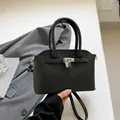 Elegante bolso de mano en cuero negro granulado con candado plateado y correa - Negro