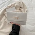 Elegant white crocodile texture clutch bag with a golden metal bow clasp in hand - White