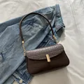 Bolso de hombro marrón oscuro con patrón de cocodrilo y cierre dorado sobre denim - Marrón