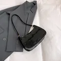 Bolso baguette negro brillante con hebilla dorada y correa fina sobre una chaqueta gris - Negro