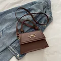 Bolso bandolera de cuero sintético marrón con lazo dorado sobre fondo denim - Marrón