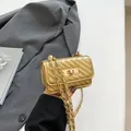 Mini gold quilted crossbody bag with chain strap and metallic finish shown in hand - Gold