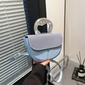 Light blue saddle bag with denim patchwork and arc silver metal handle shown in hand - Blue