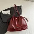 Glossy burgundy drawstring bucket bag with silver bow accent and twin shoulder straps - Red