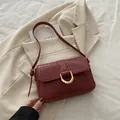 Dark red crocodile texture shoulder bag with gold D-buckle shown on beige suit - Red