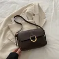 Dark brown underarm bag with crocodile texture and golden buckle on beige blazer background - Brown