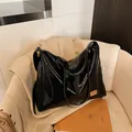 Glossy black underarm tote bag with gold metal logo on a minimalist white chair - Black