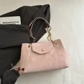 Hellrosa plissierte Schultertasche mit goldener Kette auf einem minimalistischen weißen Grund - Rosa