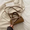 Brown faux leather shell bowling bag with metal buckle on beige blazer background - Brown