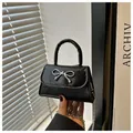 Detail of mini black handbag with lizard skin texture and silver bow decoration - Black