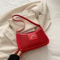 Bolso bandolera rojo trenzado con hebilla de lazo dorado sobre blazer beige - Rojo