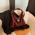 Bolso hobo retro de charol burdeos con placa metálica triangular sobre sofá beige - Rojo