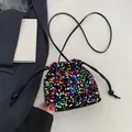 Rainbow sequin drawstring bucket bag with black strap in a stylish flat lay setting - Colorful