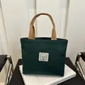 Dunkelgrüne Canvas-Handtasche mit braunen Tragegriffen und minimalistischem Bären-Aufnäher - Grün