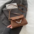 Braune Wildleder-Schultertasche mit silbernem Drehverschluss auf grauem Blazer - Braun