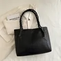 Black large tote bag with embossed star pattern and stylish braided handle on beige coat - Black