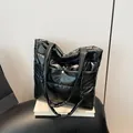 Glossy black quilted tote bag with golden buckle and padded handle on a white pedestal - Black