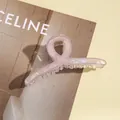 Detail einer hellrosa marmorierten Haarklammer mit goldener Feder auf einem Magazin - Hellviolett