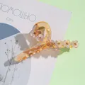 Dettaglio macro del fermaglio in resina ambrata con fiori perlati e strass scintillanti - Cioccolato