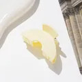Close-up of matte cream-colored small hair claw clip with cutout design on table - Off White