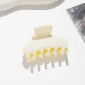 Detail shot of a matte cream-colored small hair claw clip with dense curved teeth - Off-white