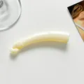 Primer plano de una pinza de pelo tipo banana en color crema con purpurina y diseño curvo - Blanco Roto