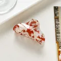 Detailansicht der rot-weißen Acetat-Haarklammer auf einem eleganten weißen Sockel - Rot