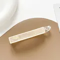 Macro view of creamy white banana hair clip with iridescent pearl texture on leather stand - Off White