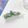 Detailed view of banana hair clip with three-petal flowers and sparkling rhinestones - Green