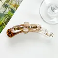 Détail d'une pince banane en résine ambrée avec fleur rose et strass marron sur le dessus - Marron