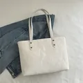 White crinkled glossy tote bag with metal rivets on textured background with denim jacket - White