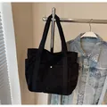 Detail of black corduroy tote bag showing front snap pocket and ribbed fabric texture - Black