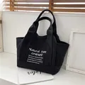 Black canvas tote bag with white lettering and side pockets for casual daily use - Black