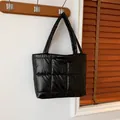 Black quilted down tote bag with a glossy finish hanging on a wooden hook in a room - Black