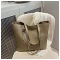 Large khaki tote bag in matte synthetic leather placed on a stylish cream office chair - Khaki
