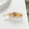 Dettaglio macro di un fermaglio a banana color champagne con fiori e perle di vetro - Giallo