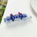 Dettaglio fermaglio a banana con strass blu e decori floreali viola su fondo bianco - Blu