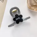 Detail of flower hair claw clip with white branding on a minimalist white table - Black Wavy Flower Decor / Gray