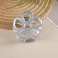 Détail d'une pince à cheveux fleur évidée argent mat sur un plateau en bois épuré - Gris