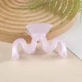 Détail macro d'une pince à cheveux rose ondulée avec finition nacrée sur plateau bois - Violet
