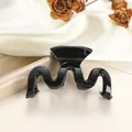 Detalle macro de pinza de pelo negra ondulada sobre seda blanca y plato de cerámica - Negro Puro