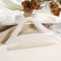 Nahaufnahme der perlweißen Dreieck-Haarklammer mit goldener Feder auf Satin-Stoff - Milchweiß