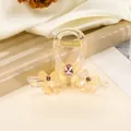Close-up of champagne resin hair claw clip with pink rhinestones and gold spring detail - Yellow