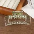 Close-up of translucent green floral hair claw with crystals on wooden stand - Green
