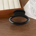 Glossy black oval hair claw clip with mirror finish on a minimalist wooden display - Black