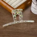 Gros plan d'une pince à cheveux en acrylique à motif floral sur un support en bois - Vert