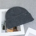 Detail shot of a dark grey wool knit beanie featuring a square logo patch on a textured surface - One Size(Elastic) / Dark Gray