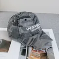 Dettaglio del cappello camouflage con lettere ricamate e bordi usurati per uno stile street - Regolabile / Mimetico