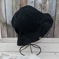Détail d'un chapeau de soleil en coton noir avec dos élastique et étiquette marron - Réversible / Noir + Kaki