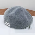 Detailed texture of dark gray wool newsboy cap with silver metallic brand logo tag - Adjustable / Gray